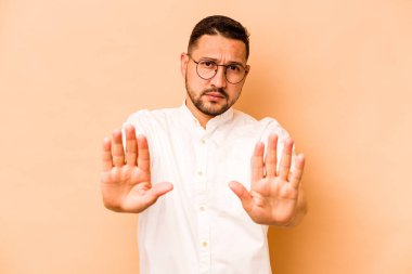Latin kökenli genç bir adam, bej arka planda izole edilmiş, elini uzatmış, dur işareti göstererek seni engelliyor..