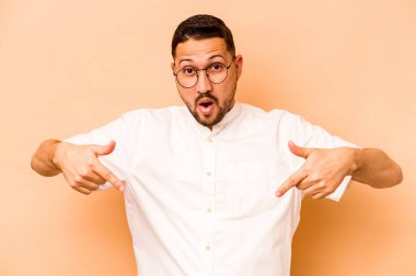 Latin kökenli genç adam bej arka planda izole edilmiş. Parmakları aşağıda, olumlu hisler içinde..