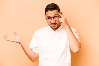 Latin kökenli genç adam bej arka planda izole edilmiş işaret parmağıyla hayal kırıklığı jesti gösteriyor..