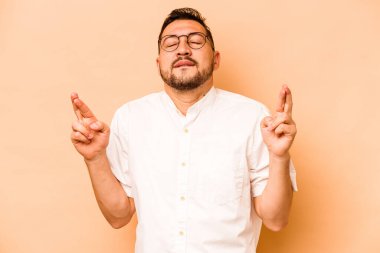 Latin kökenli genç adam, şans dilemek için bej arka planda izole edilmiş.