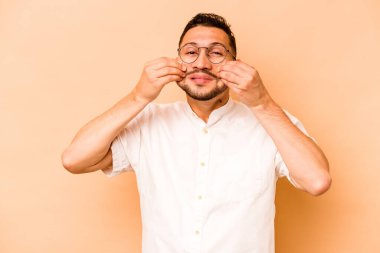 Latin kökenli genç bir adam bej arka planda iki seçenek arasında kuşkulanıyor..