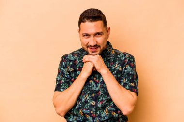 Bej arka planda izole edilmiş genç İspanyol adam ellerini çenesinin altında tutuyor ve mutlu bir şekilde yan tarafa bakıyor..