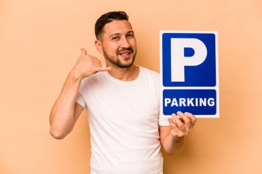 İspanyol beyaz adam, elinde bej arka planda izole edilmiş park plakası tutarken, parmakları olan bir cep telefonu hareketi gösteriyor..