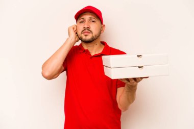 Elinde pizza tutan genç teslimatçı bej arka planda izole edilmiş kulakları elleriyle kapatıyor..