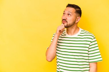 Genç İspanyol adam sarı arka planda izole edilmiş şüpheli ve şüpheci bir ifadeyle yana bakıyor..