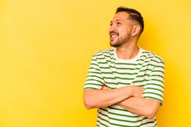 Sarı arka planda izole edilmiş genç İspanyol adam kollarını kavuşturarak gülümsüyor..