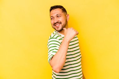 Latin kökenli genç adam sarı arka planda izole edilmiş, başparmak uzakta, gülüyor ve kaygısız..