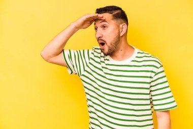 Genç İspanyol adam sarı arka planda izole edilmiş, uzaklara bakıyor ve elini alnına koyuyor..