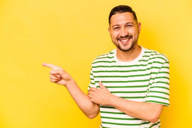 Sarı arka planda izole edilmiş genç İspanyol adam işaret parmağıyla işaret ederek gülümsüyor..