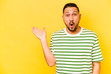 Sarı arka planda izole edilmiş genç İspanyol adam, avuç içinde kopya alanı tutmaktan etkilenmiş..