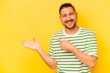 Sarı arka planda izole edilmiş genç İspanyol bir adam heyecanlı bir şekilde avuç içinde bir kopyasını tutuyor..