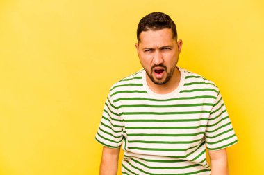 İspanyol asıllı genç adam sarı arka planda izole edilmiş çok kızgın, öfkeli, hayal kırıklığına uğramış bağırıyor..