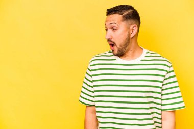 Genç İspanyol adam sarı arka planda izole edilmiş. Gördüğü bir şey yüzünden şoka uğruyor..