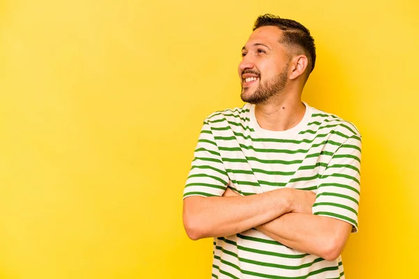Young hispanic man isolated on yellow background smiling confident with crossed arms.