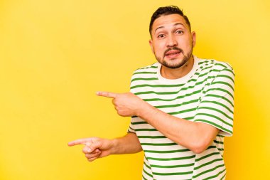 Sarı arka planda izole edilmiş genç İspanyol adam işaret parmağıyla fotokopi alanını işaret ederek şok oldu..