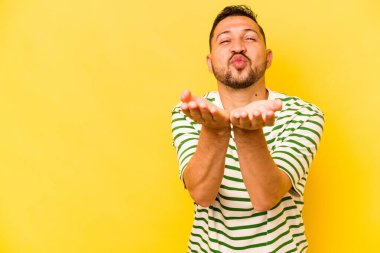 Sarı arka planda izole edilmiş, dudakları kıvrılmış ve hava öpücüğü yollamak için avuç içi tutan İspanyol bir adam..
