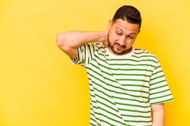 Genç İspanyol bir adam sarı arka planda izole edilmiş kafasının arkasına dokunuyor, düşünüyor ve bir seçim yapıyor..