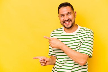 Sarı arka planda izole edilmiş genç İspanyol adam işaret parmaklarıyla fotokopi alanını işaret ederek heyecan ve arzuyu ifade ediyor..