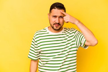 Sarı arka planda izole edilmiş genç İspanyol bir adam şakağı parmağıyla işaret ediyor, düşünüyor ve bir göreve odaklanıyor..