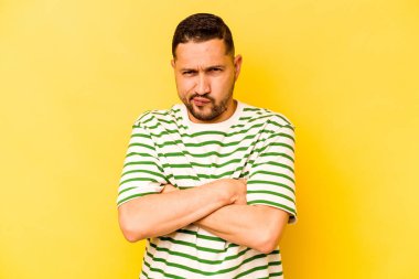 Sarı arka planda izole edilmiş, hoşnutsuzca kaşlarını çatmış, kollarını kavuşturmuş genç bir İspanyol..