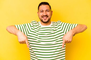 Latin kökenli genç adam sarı arka planda izole edilmiş. Parmakları aşağıda, olumlu hisler içinde..