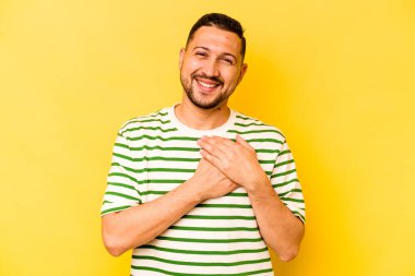 Sarı arka planda izole edilmiş genç İspanyol bir adam dost canlısı bir ifadeye sahip, avuçlarını göğsüne bastırıyor. Aşk konsepti.