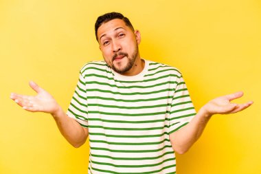 Latin kökenli genç bir adam sarı arka planda izole edilmiş. Sorgulama sırasında omuz silkiyor ve şüphe duyuyor..