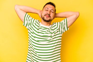 İspanyol genç adam sarı arka planda izole edilmiş. Kendine güveniyor, elleri başının arkasında..