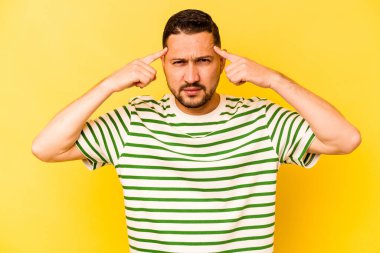 Sarı arka planda izole edilmiş genç İspanyol adam bir göreve odaklanmış, işaret parmaklarını işaret ediyor..