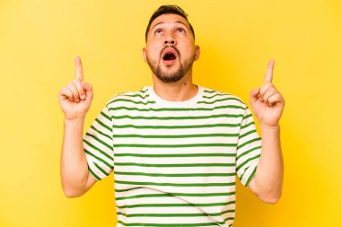 Sarı arka planda izole edilmiş genç bir İspanyol ağzı açık bir şekilde yukarı işaret ediyor..