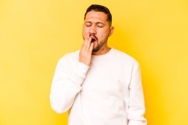 Sarı arka planda izole edilmiş genç İspanyol adam esniyor. Ağzı eliyle kapatan yorgun bir hareket sergiliyor..