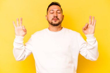 Sarı arka planda izole olmuş genç İspanyol adam sıkı çalışma gününden sonra rahatlıyor. Yoga yapıyor..