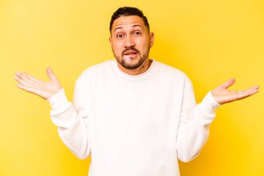 Sarı arka planda izole edilmiş genç İspanyol bir adam. Kafası karışmış ve omuz silkiyor. Kopya alanını tutmak için..