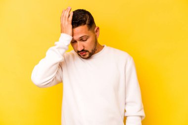 Sarı arka planda izole edilmiş genç bir İspanyol. Çok yorgun ve uykulu. Elini başının üstünde tutuyor..