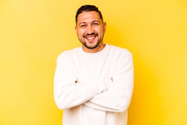 Sarı arka planda kendini güvende hisseden, kararlılıkla kollarını kavuşturan genç İspanyol bir adam..