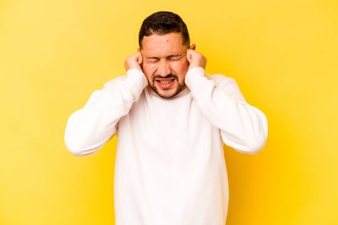 Sarı arka planda izole edilmiş genç bir İspanyol. Kulakları elleriyle kapatıyor..