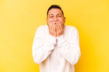 Sarı arka planda izole edilmiş genç İspanyol bir adam bir şeye gülüyor, elleriyle ağzını kapatıyor..