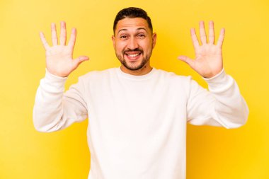 Sarı arka planda izole edilmiş genç İspanyol adam on numarayı elleriyle gösteriyor..
