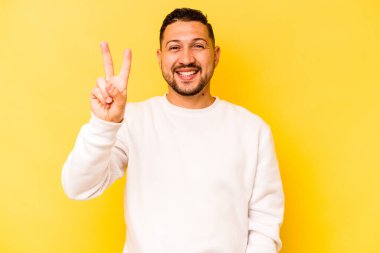 Sarı arka planda izole edilmiş genç İspanyol adam neşeli ve kaygısız parmakları olan bir barış sembolü gösteriyor..