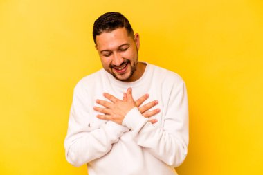 Sarı arka planda izole edilmiş genç İspanyol adam mutlu bir şekilde gülüyor ve ellerini karnının üstünde tutarak eğleniyor..