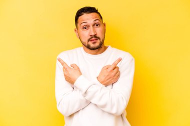 Sarı arka plan noktalarında izole edilmiş genç İspanyol adam iki seçenek arasında seçim yapmaya çalışıyor..