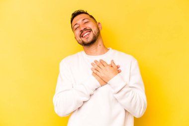 Sarı arka planda izole olmuş genç İspanyol adam gülüyor, ellerini kalbe koyuyor, mutluluk kavramını koruyor..