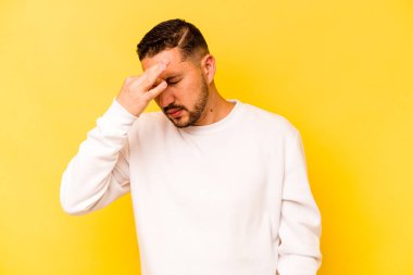 Sarı arka planda izole edilmiş genç İspanyol bir adamın başı ağrıyor, yüzüne dokunuyor..