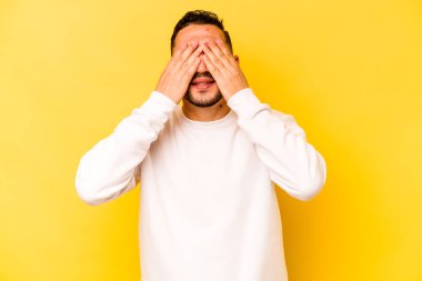 Sarı arka planda izole edilmiş genç İspanyol adam elleriyle gözlerini kapatmaktan korkuyor..