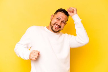 Sarı arka planda izole edilmiş genç İspanyol özel bir günü kutluyor, atlıyor ve enerjiyle kollarını kaldırıyor..