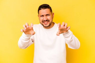 Sarı arka planda izole edilmiş genç İspanyol bir adam pençelerini bir kediyi taklit ederken gösteriyor, agresif bir hareket..