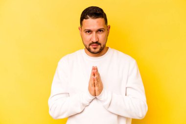 İspanyol asıllı genç adam sarı arka planda izole edilmiş dua ediyor, bağlılık gösteriyor, dindar biri ilahi ilhamı arıyor..