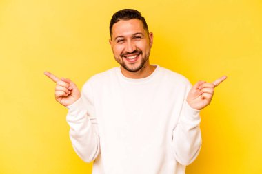 Sarı arka planda izole edilmiş genç İspanyol adam farklı kopya alanlarını gösteriyor, birini seçiyor, parmaklarıyla gösteriyor.