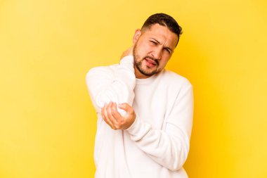 Genç İspanyol adam sarı arka planda izole edilmiş dirsek masajı yapıyor, kötü bir hareketin ardından acı çekiyor..