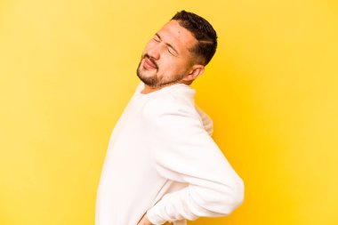 Genç İspanyol adam sarı arka planda izole edilmiş sırt ağrısı çekiyor..